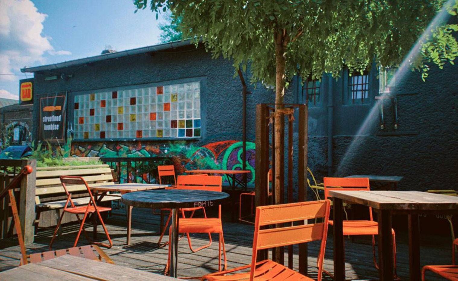 verschiedene orange Stühle und Holztische in der Sonne auf einer Terrasse stehend
